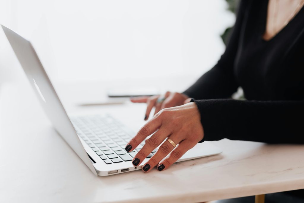 A person types diligently on a laptop at a sleek desk, dressed in a dark long-sleeve shirt. They're immersed in navigating the corporate training platform, seamlessly blending professionalism with innovation.